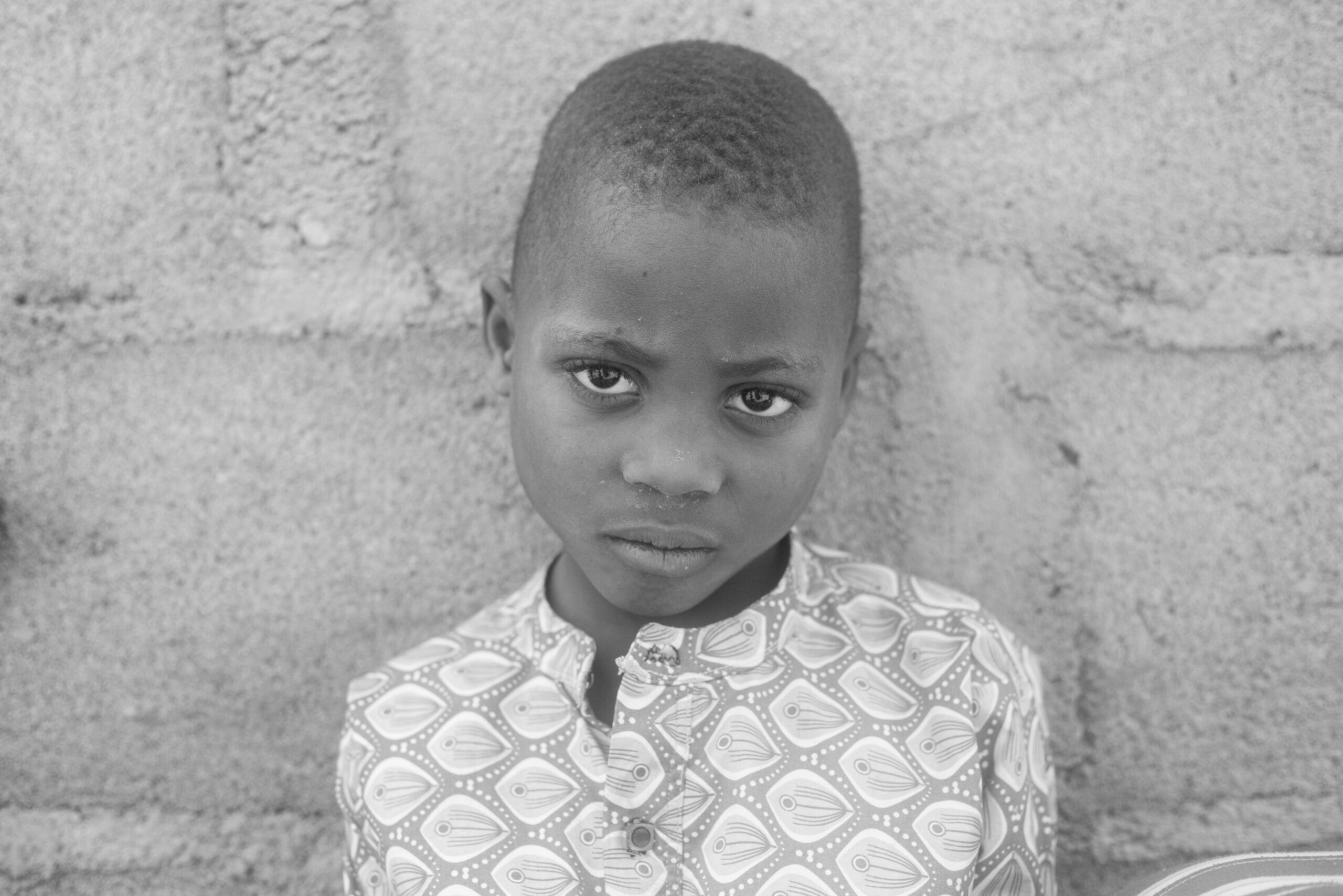 a black and white image of a girl child leaning on a wall. She is sad